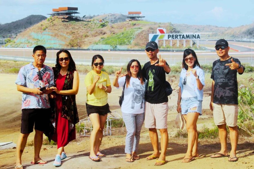A group of people posing in front of a sign that reads 'PERTAMINA' with a hilly landscape in the background. 5