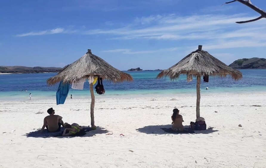 A beach with two thatched umbrellas, a sandy shore, and calm blue waters. 2