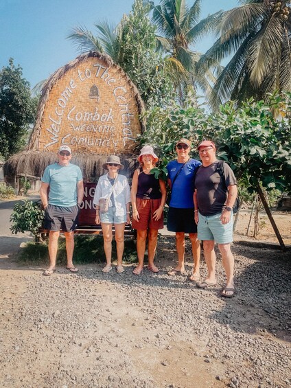 A group of people standing in front of a thatched structure with a welcome sign. 3