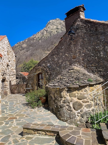 A stone pathway leading to a rustic building with a wooden gate and a mountain backdrop. 2