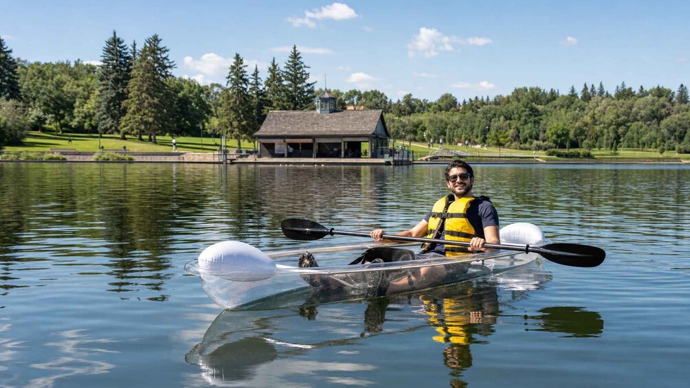 A person kayaking on a calm lake with a house and trees in the background. 4