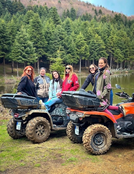 A group of people on all-terrain vehicles (ATVs) in a forested area with a lake in the background. 5