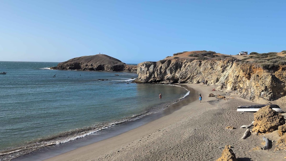 A beach with rocky cliffs, calm sea, and a few people walking along the shore. 5