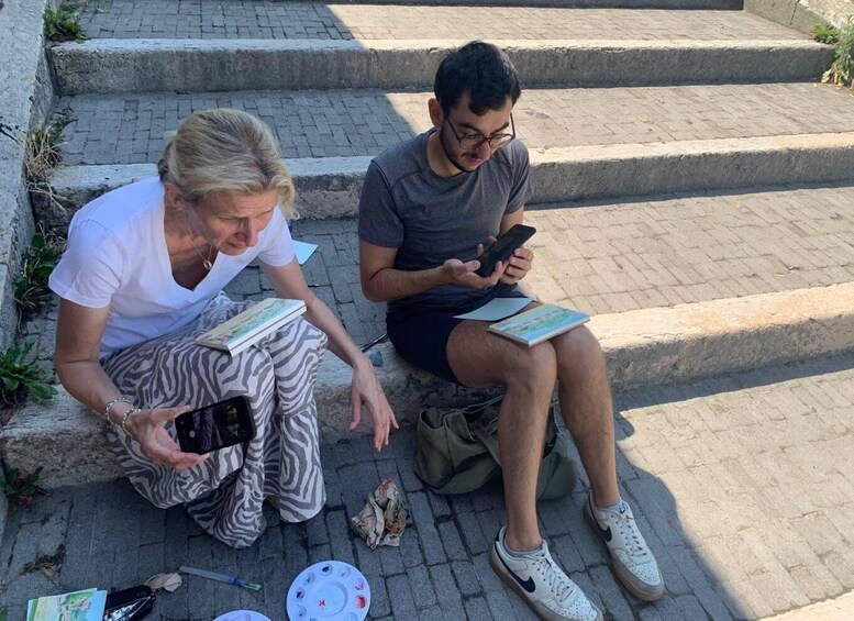 Two people sitting on steps, one holding a smartphone and the other holding a book. 4