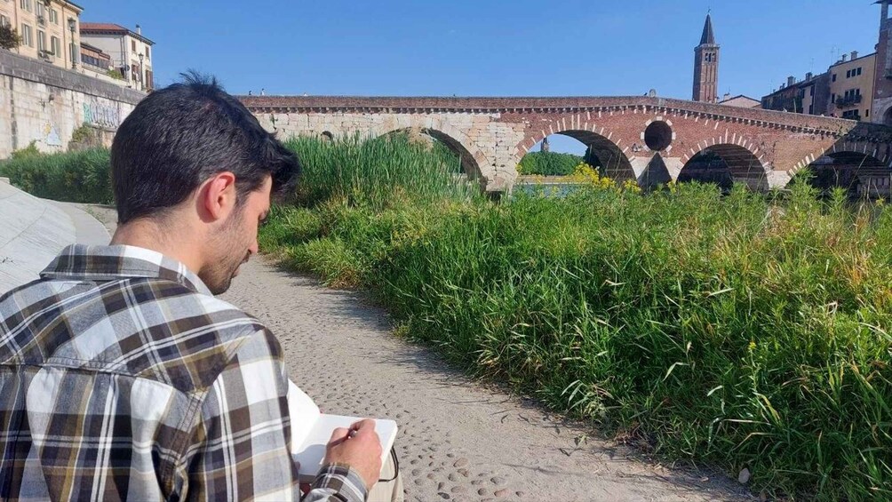A man reading a book on a path with a bridge and a tower in the background. 3