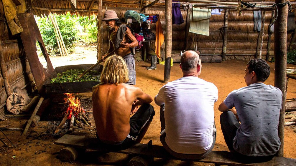 A rustic outdoor setting with a fire, wooden structures, and people engaged in an activity. 4