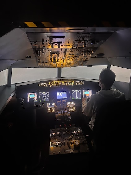 A cockpit with multiple screens and controls, a person in a hoodie, and a view of the sky through the windshield. 3