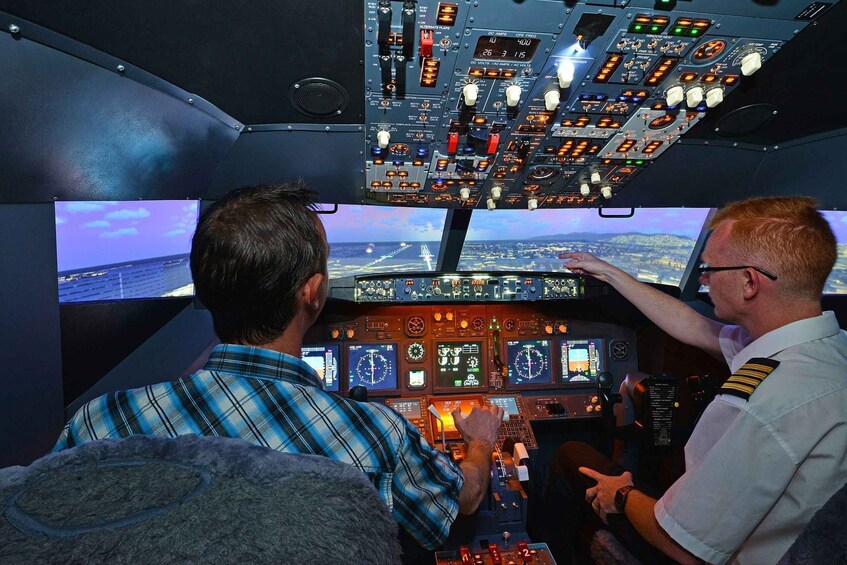 Two individuals in a cockpit with multiple control panels and screens displaying flight information. 5