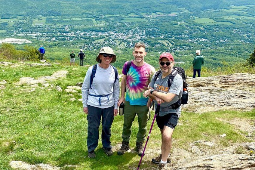Three people standing on a grassy hill with a scenic view of a valley in the background. 4