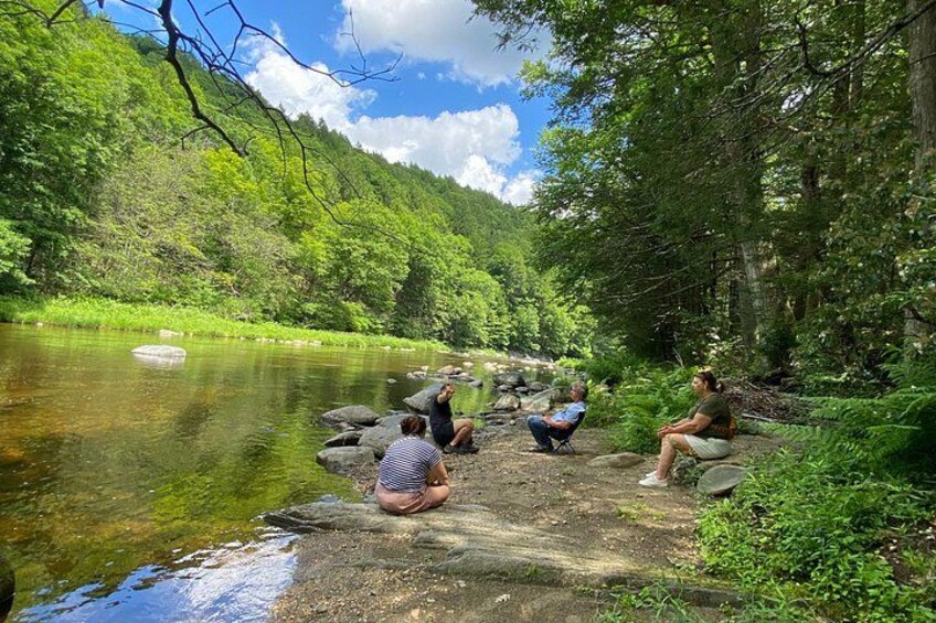 A group of people sitting on rocks by a river surrounded by lush greenery. 3