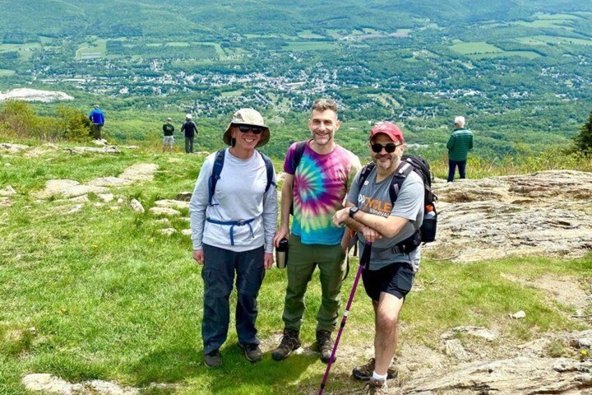 Three people hiking on a grassy hill with a scenic view of a valley below. 2