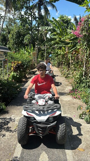 A person riding a quad bike on a paved path surrounded by lush tropical vegetation. 2