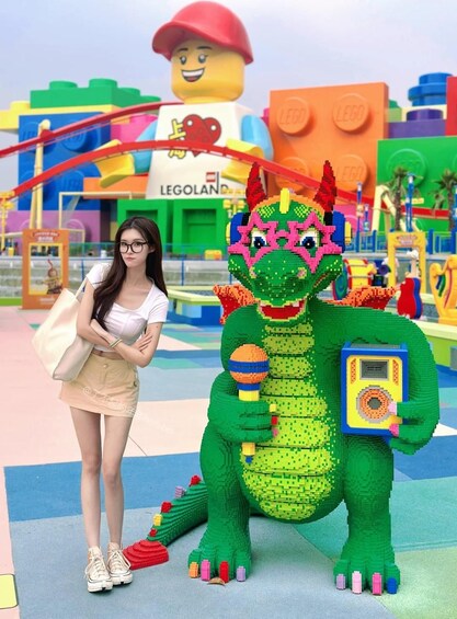 A person standing next to a LEGO dinosaur in a colorful play area with a LEGO figure in the background. 4