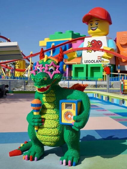A LEGO dinosaur statue holding a microphone and a sign, with a LEGO figure in the background and a LEGOland sign. 2