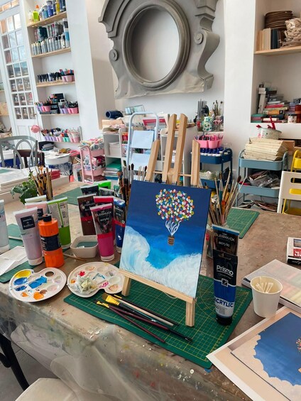 An art studio with a painting of a heart-shaped balloon on a canvas, surrounded by art supplies and tools. 2