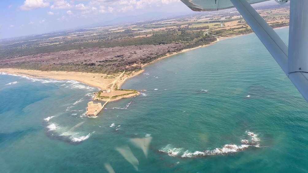An aerial view of a coastal area with a sandy beach, a small island with a structure, and a clear blue sea. 4
