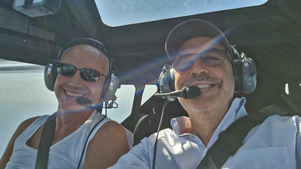 Two people in a cockpit with headsets, one wearing a white tank top and the other a striped shirt. 3