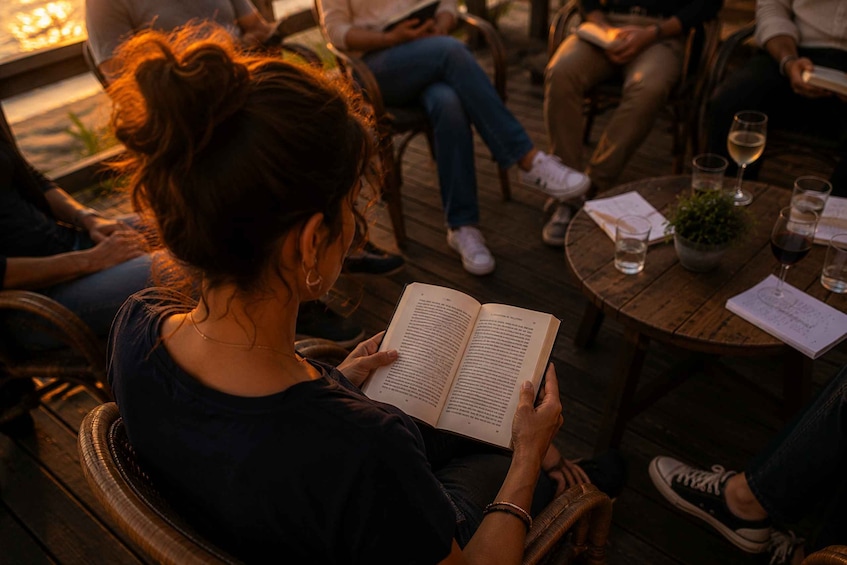 A person reading a book at a wooden table with drinks and a plant. 3