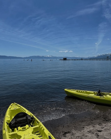 A calm lake with kayaks on the shore, a pier extending into the water, and mountains in the background. 5