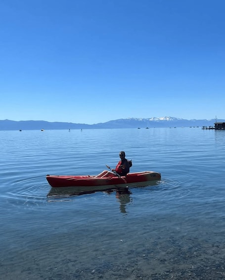 A person in a red kayak on calm water with mountains in the background. 3