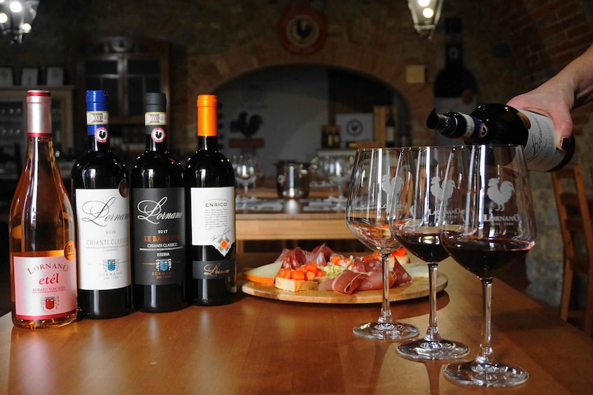 A selection of wine bottles and glasses on a wooden table, with a person pouring wine into one of the glasses. 2