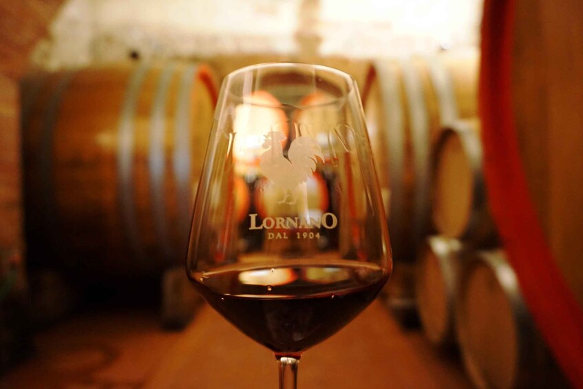 A wine glass with a dark liquid, possibly wine, in a dimly lit setting with barrels in the background. 1