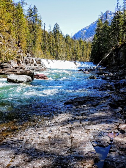 A river flowing through a rocky landscape with trees and mountains in the background. 2