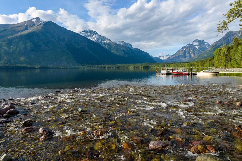 A calm lake with clear water, surrounded by mountains and a boat docked on the shore. 1
