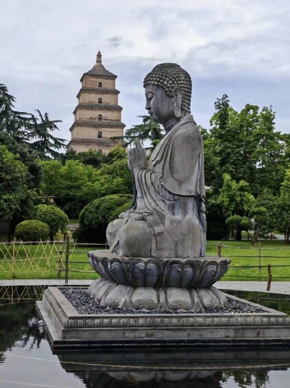 A large Buddha statue on a lotus pedestal in a park with a pagoda in the background. 3