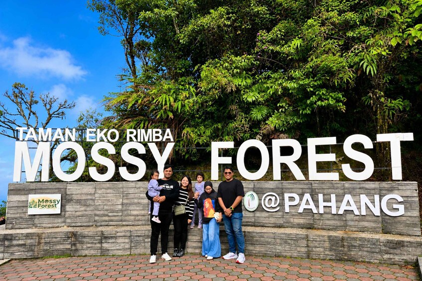 A group of people standing in front of a sign that reads 'TAMAN EKO RIMBA MOSSY FOREST @PAHANG'. 2