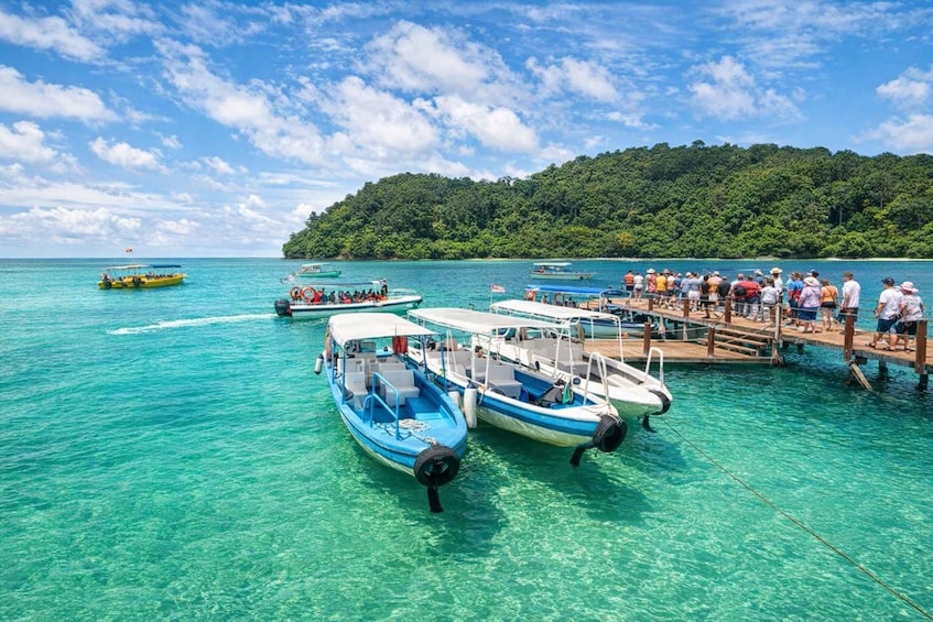 A clear turquoise sea with boats docked at a pier, surrounded by lush green hills. 1