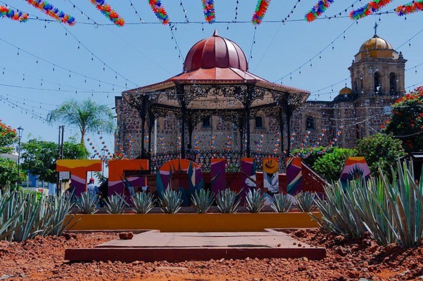 A colorful gazebo with a red dome, surrounded by decorative elements and a building with a dome in the background. 1