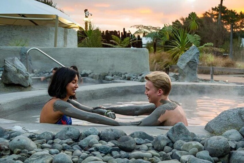 Two people in a hot spring with rocks and a sunset in the background. 5