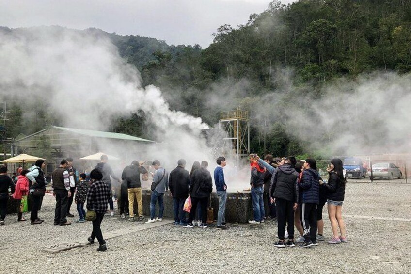 A group of people gathered around a steam vent, with steam rising into the air. 4