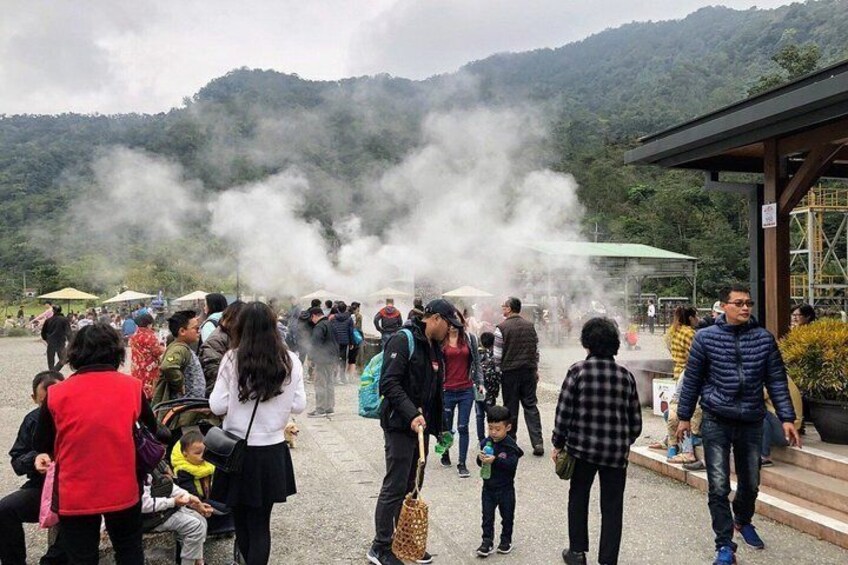 A group of people gathered around a steam vent, with a mountainous backdrop. 5