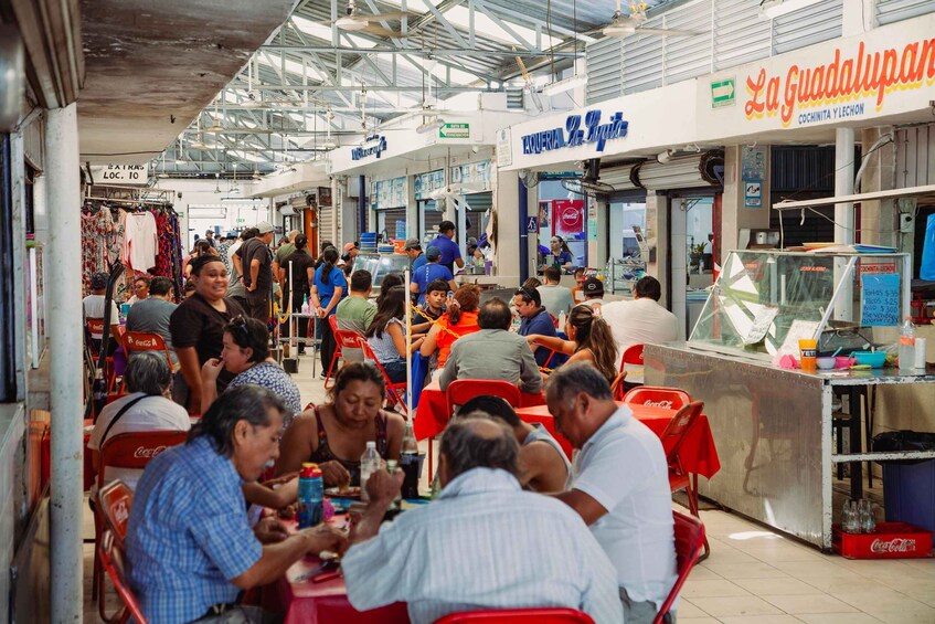 A busy outdoor market with people dining at tables, a Coca-Cola vending machine, and a sign for La Guadalupana. 2