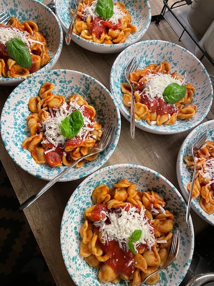 Multiple bowls of pasta with tomato sauce, grated cheese, and basil leaves. 1
