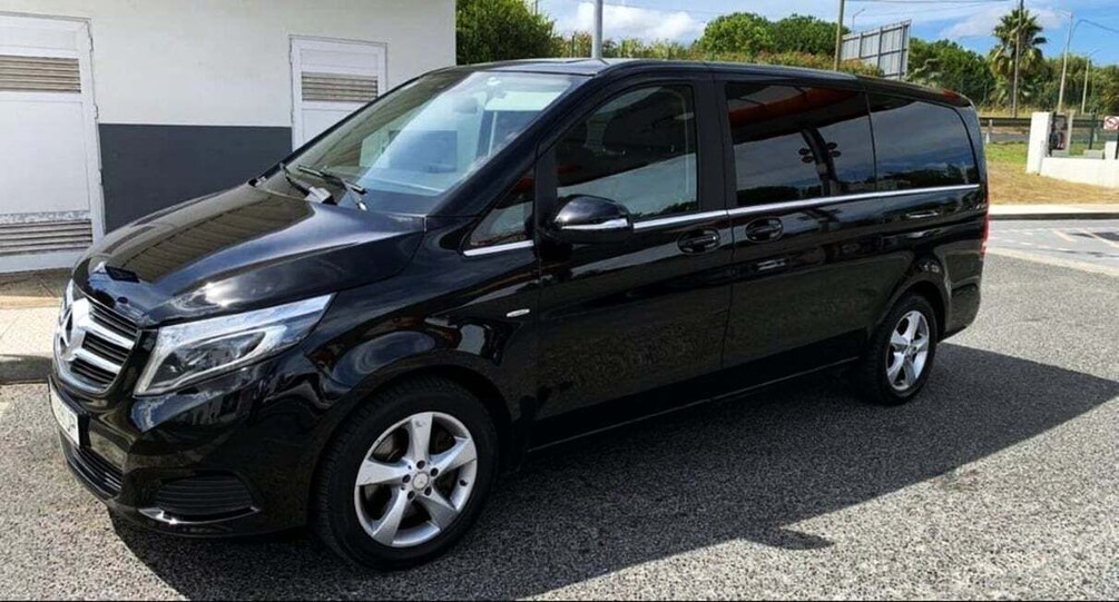 A black minivan parked on a gravel surface with a building in the background. 2