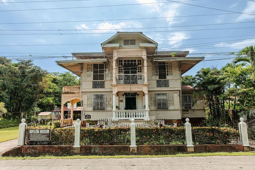 A historic building with a balcony, surrounded by a fence and a sign for the Hofilena Museum. 5