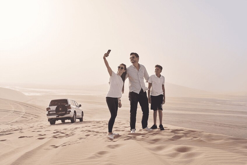 A group of people taking a selfie with a desert landscape and a vehicle in the background. 3
