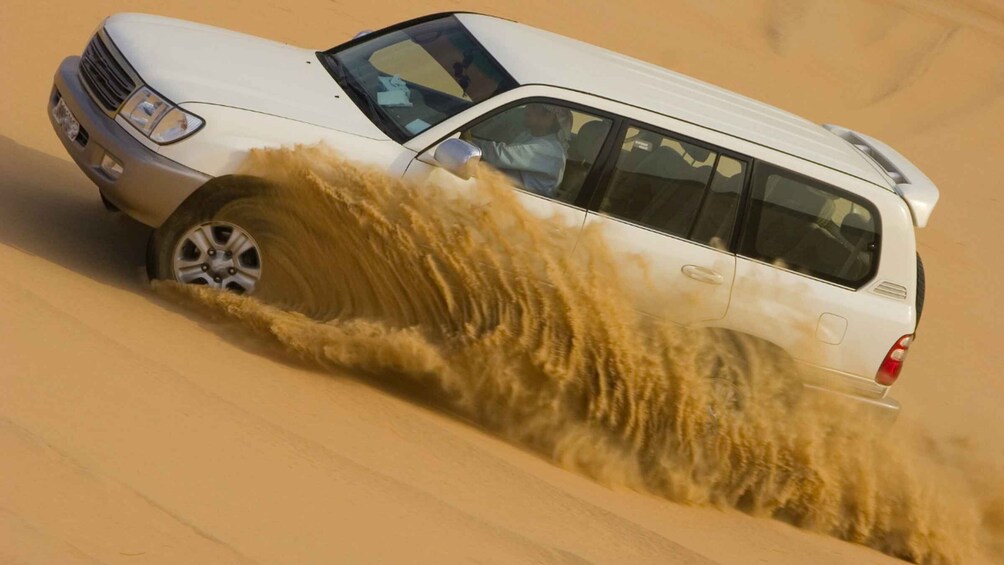 A white SUV driving through a sandy desert with a large dust cloud behind it. 4