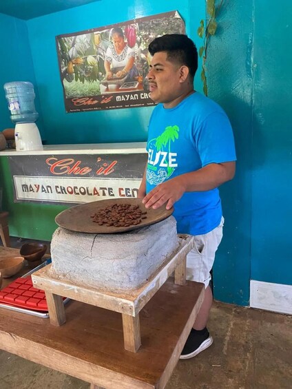 A person standing next to a traditional Mayan chocolate making setup with a stone grinder and cocoa beans. 1