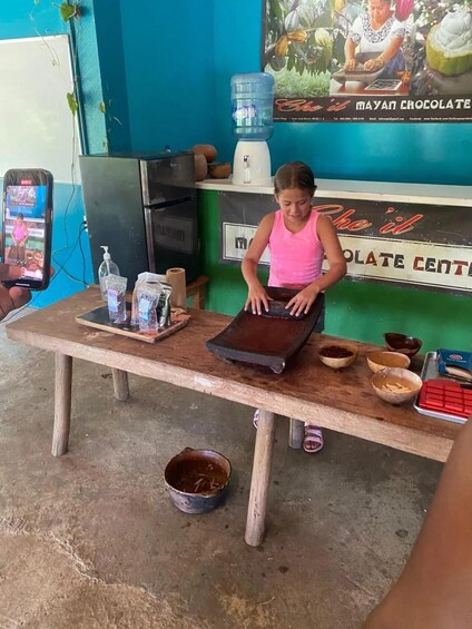 A person working at a wooden table with a chocolate-making setup, including bowls and a water dispenser. 2