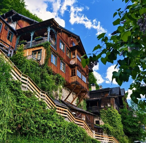 A multi-story wooden house with balconies, surrounded by lush greenery and a clear blue sky. 5