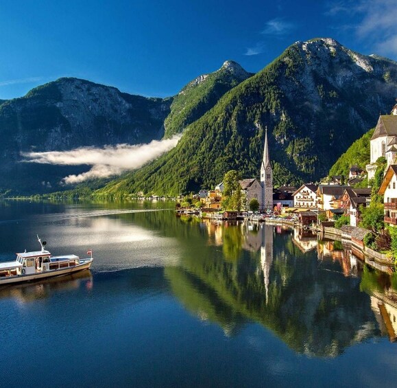 A lake with a boat, a church, and houses surrounded by mountains. 1