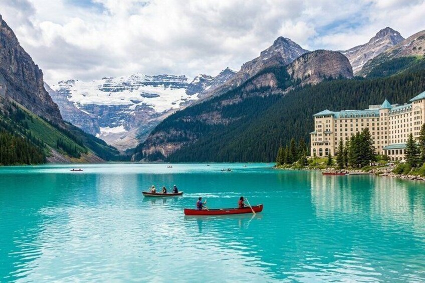 A calm lake with boats, a mountain range, and a lodge. 1