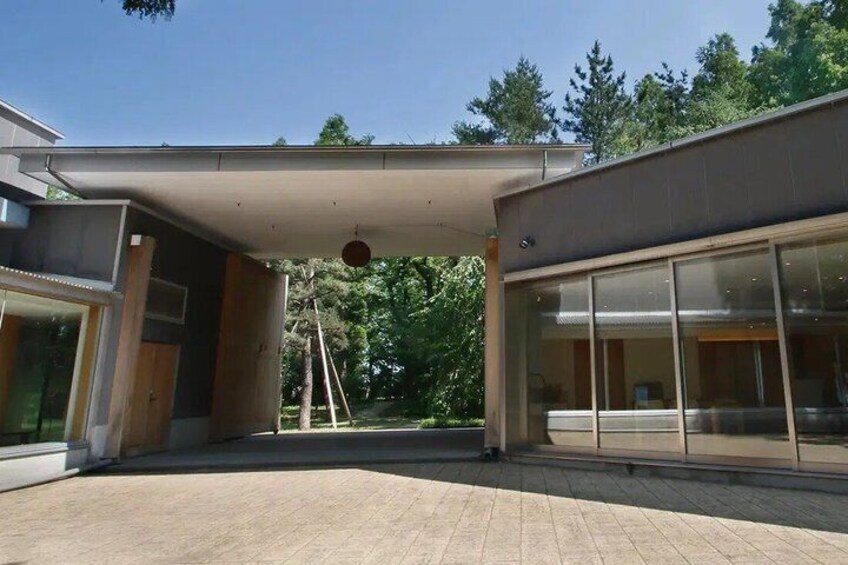 A modern building with large glass windows, a covered walkway, and a paved area. 2