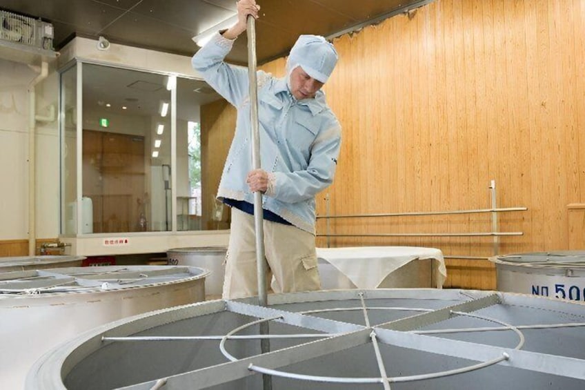 A person in a white chef's coat and hat, standing in a kitchen with a large circular cooking apparatus. 1