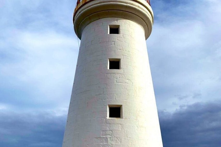 A tall, cylindrical lighthouse with three windows and a weathered exterior. 1