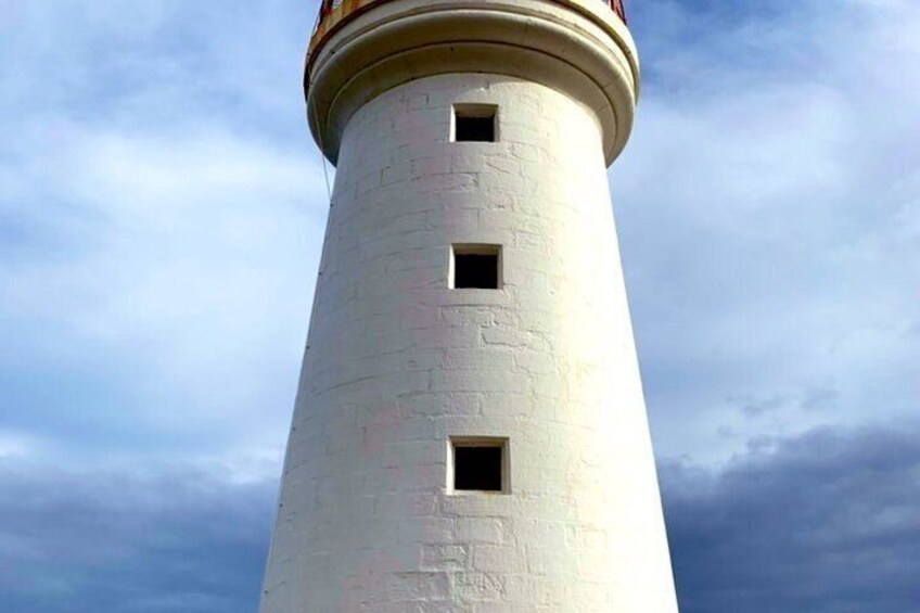 A tall white lighthouse with three windows and a red roof against a cloudy sky. 1